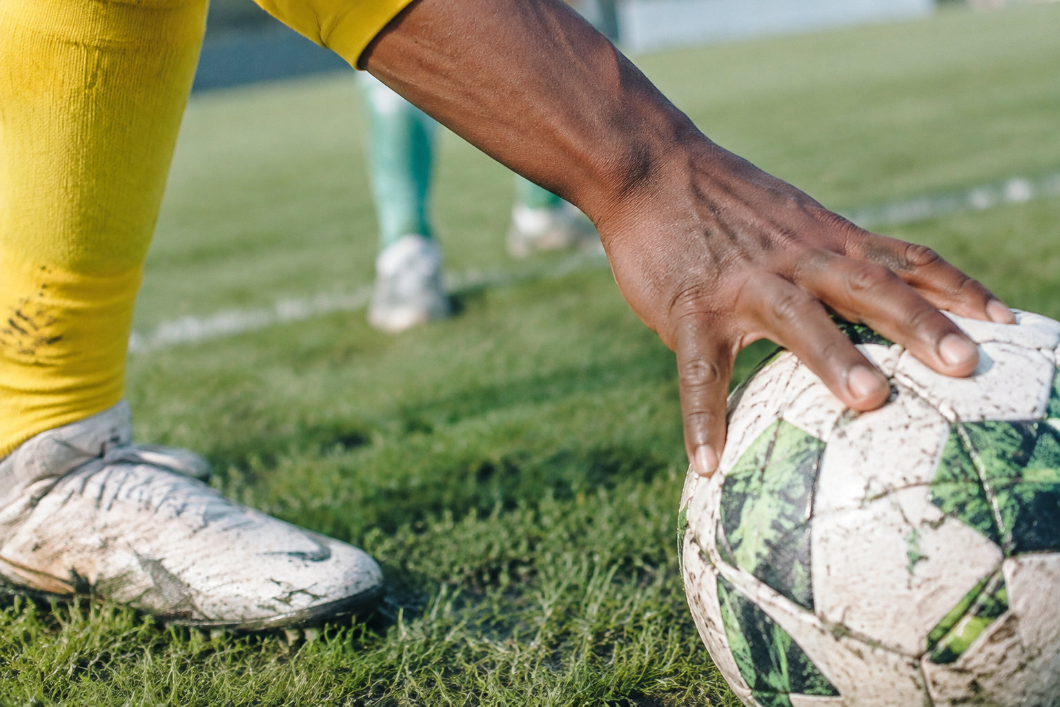 Gros plan sur la main d'un joueur portant une chaussette jaune, posant un ballon de football sur la pelouse.